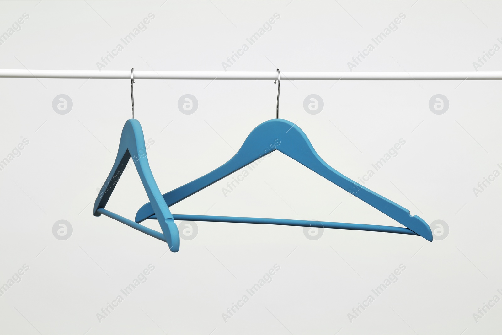 Photo of Empty clothes hangers on metal rail against light background