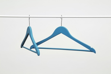 Empty clothes hangers on metal rail against light background