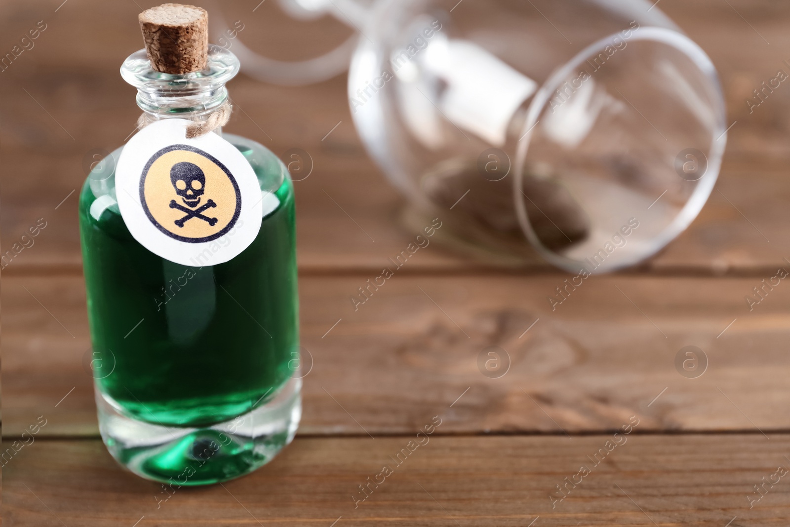 Photo of Bottle of poison and partially emptied glass on wooden table