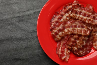 Photo of Plate with fried bacon slices on dark textured table, top view. Space for text