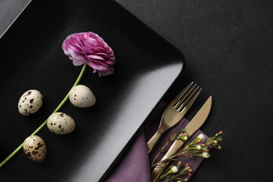 Festive Easter table setting with quail eggs and floral decoration on dark background, flat lay
