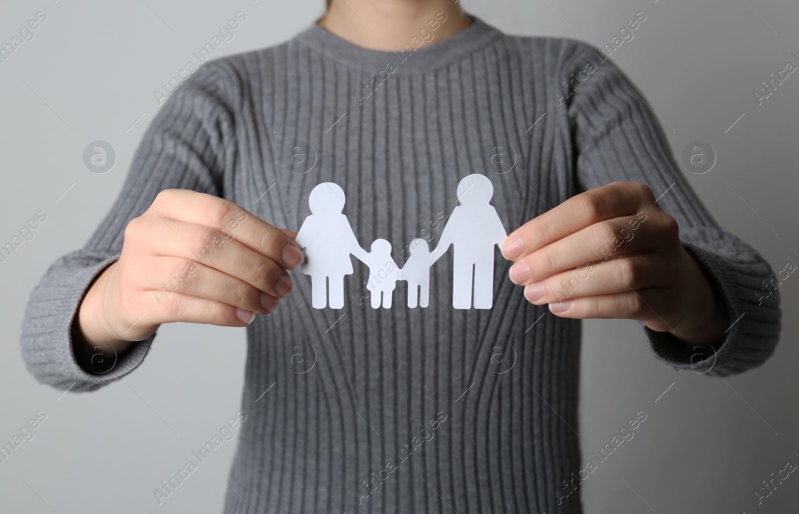 Photo of Woman holding paper silhouette of family on grey background, closeup. Life insurance concept