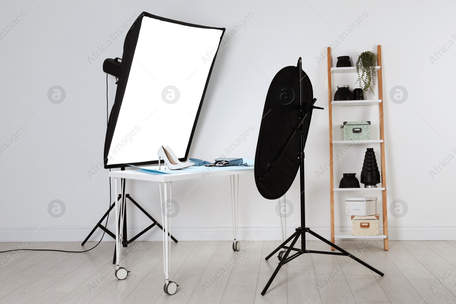 Photo of Professional lighting equipment near table with fashionable women's shoes and accessories in photo studio