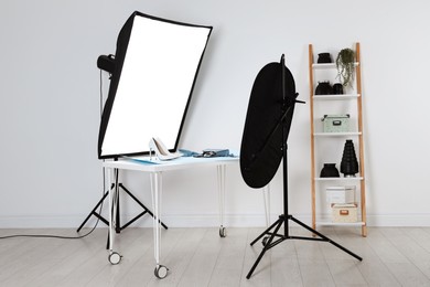 Professional lighting equipment near table with fashionable women's shoes and accessories in photo studio