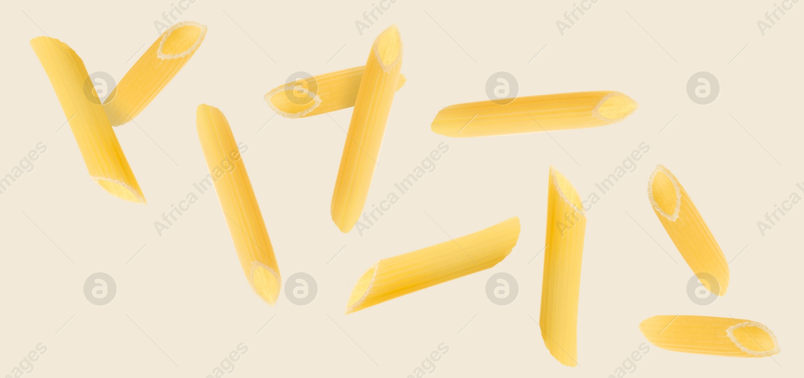 Image of Raw penne pasta flying on beige background
