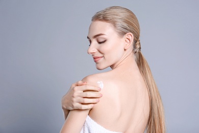 Photo of Young woman applying body cream on color background