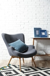 Photo of Modern interior with cozy armchair and table near brick wall