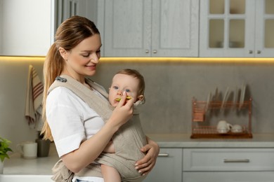 Photo of Mother feeding her cute child in sling (baby carrier) at home