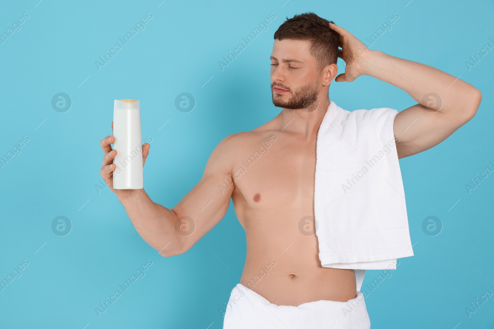 Photo of Shirtless young man holding bottle of shampoo on light blue background