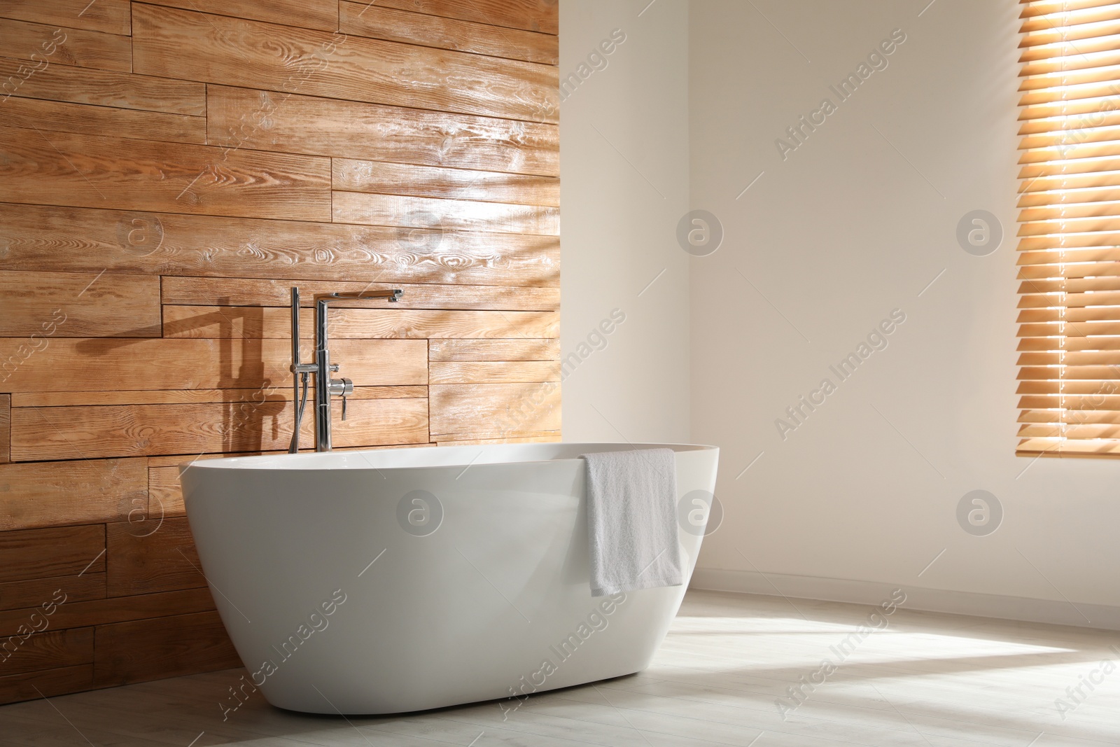 Photo of White bathtub with towel near wooden wall in room