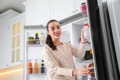 Photo of Young woman taking yoghurt out of refrigerator in kitchen, low angle view