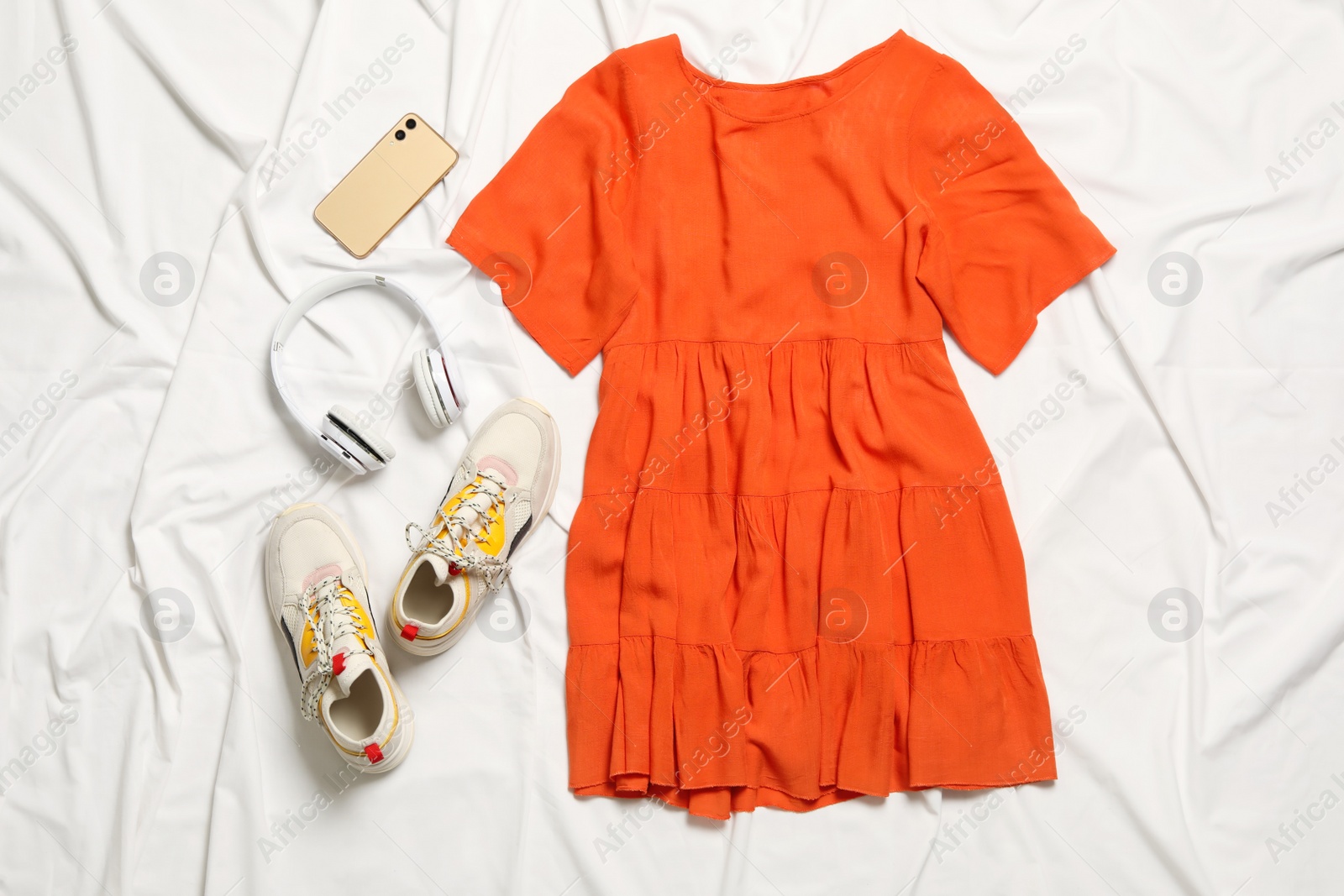 Photo of Flat lay composition with stylish orange dress on white fabric