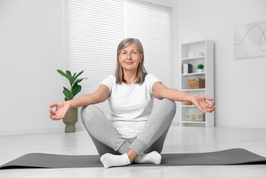 Photo of Happy senior woman practicing yoga on mat at home