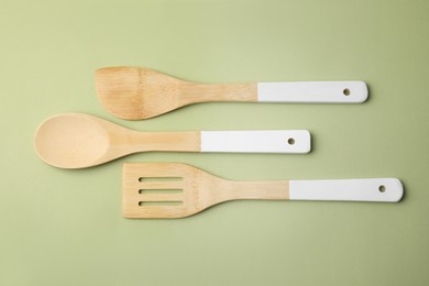 Wooden kitchen utensils on light olive background, flat lay