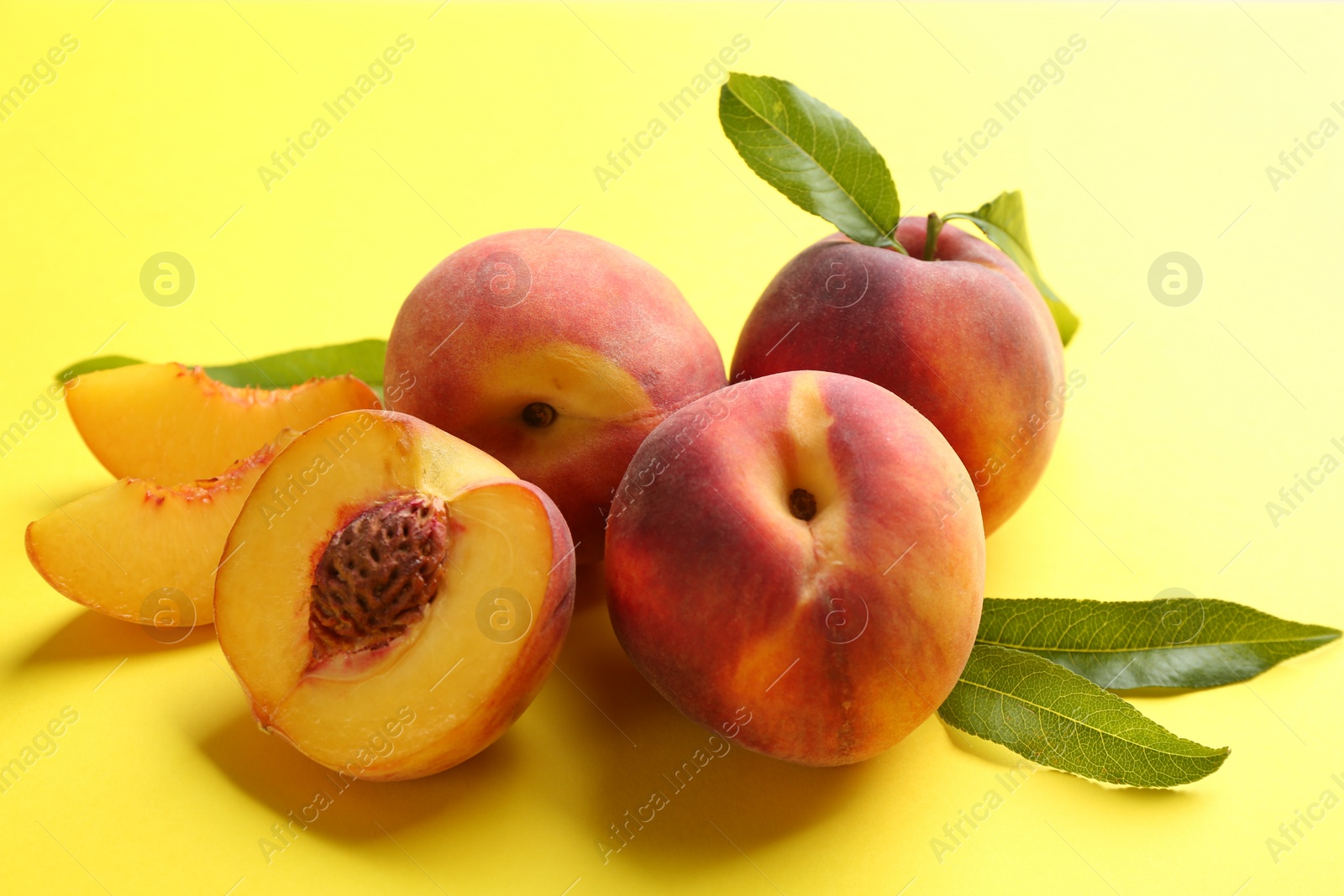 Photo of Fresh ripe peaches and green leaves on yellow background, closeup
