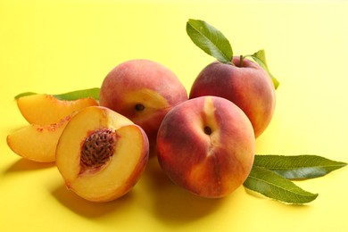 Photo of Fresh ripe peaches and green leaves on yellow background, closeup