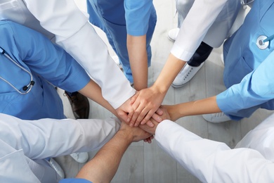 Photo of Team of medical workers holding hands together indoors, top view. Unity concept