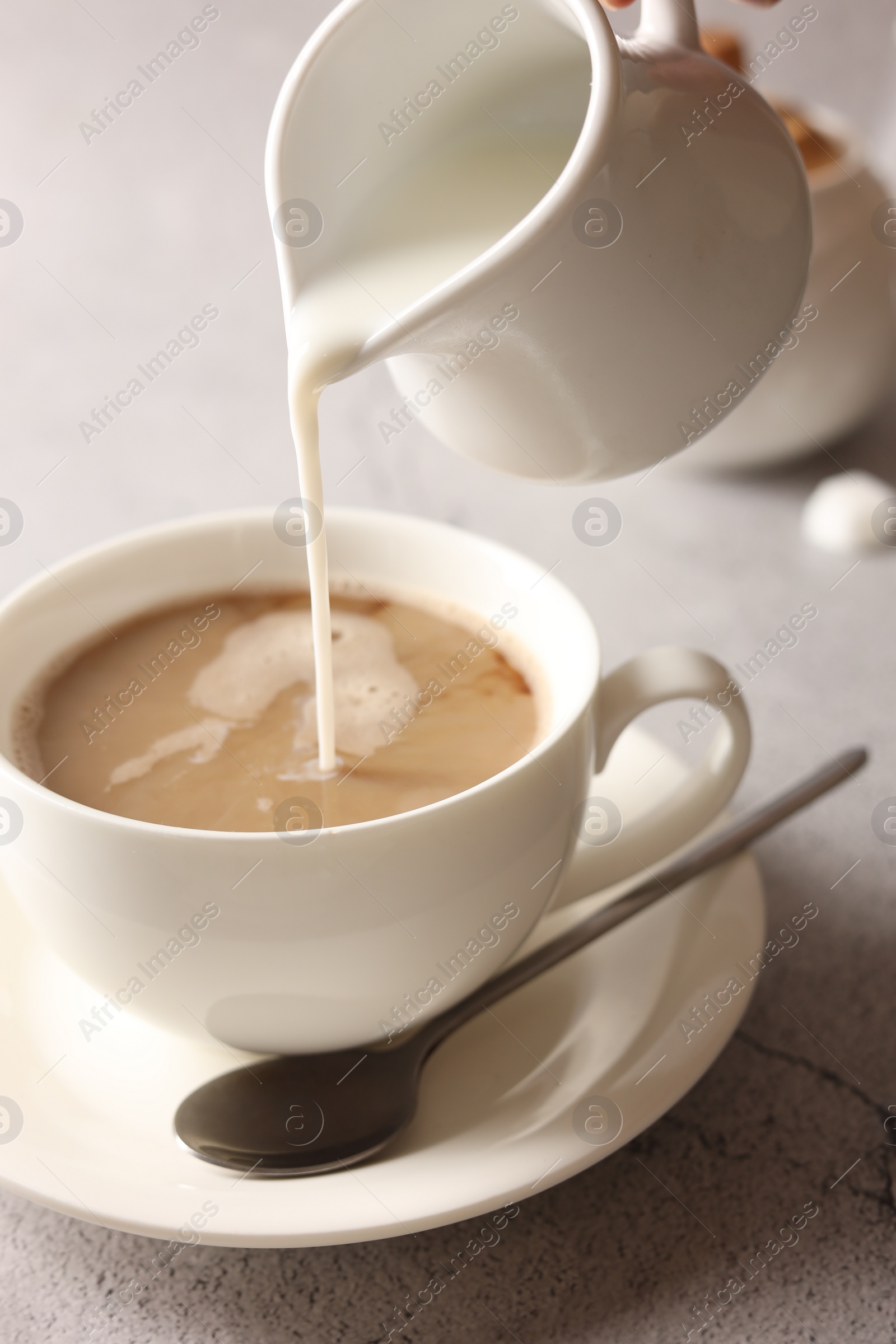 Photo of Pouring milk into cup with coffee on light grey textured table, closeup