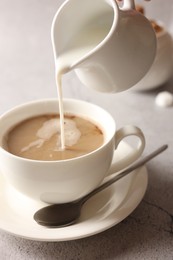 Photo of Pouring milk into cup with coffee on light grey textured table, closeup