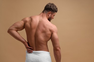 Photo of Man suffering from back pain on beige background, back view. Space for text