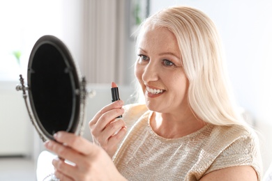 Photo of Mature woman applying makeup in front of mirror at home