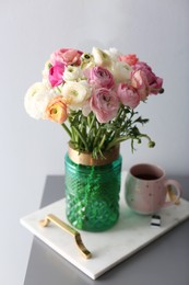 Photo of Bouquet of beautiful ranunculuses and tea on table near light grey wall