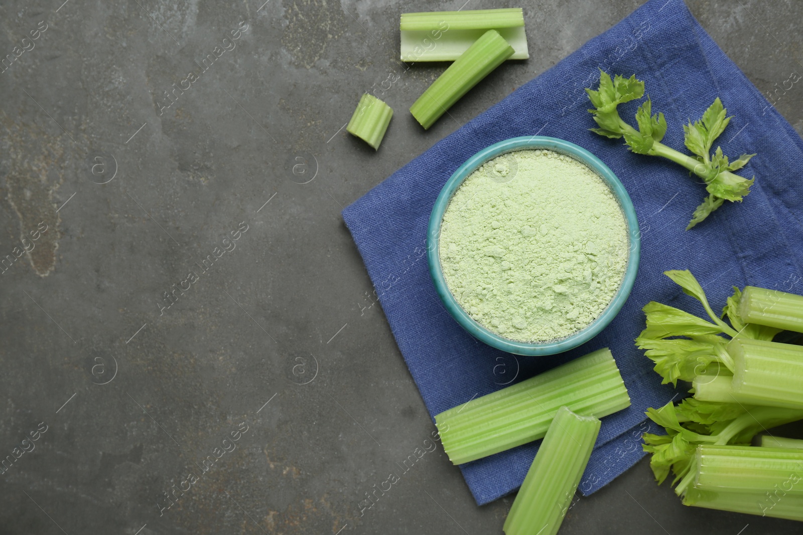 Photo of Natural celery powder in bowl and fresh stalks on grey table, flat lay. Space for text