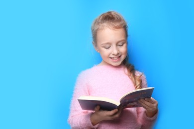 Happy little girl reading book on light blue background. Space for text