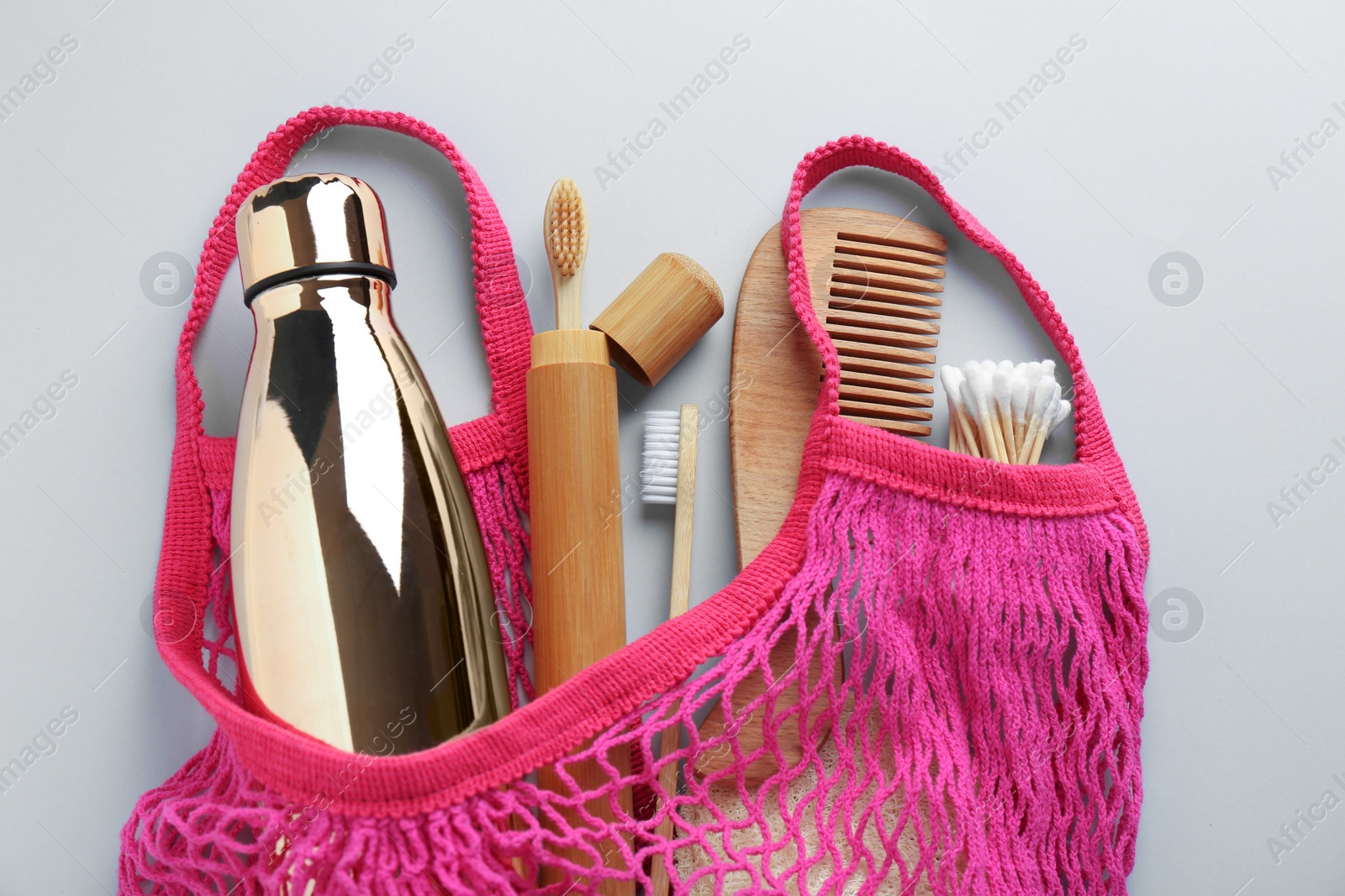 Photo of Fishnet bag with different items on light grey background, top view. Conscious consumption