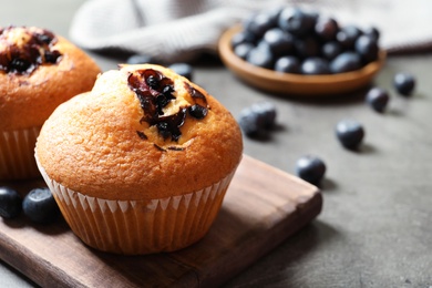 Photo of Wooden board with blueberry muffins on grey table, closeup view. Space for text