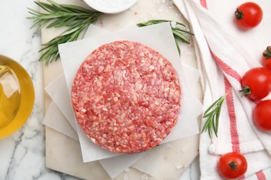 Photo of Raw hamburger patties with rosemary, salt and tomatoes on white marble table, flat lay