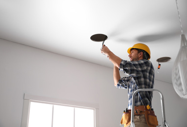 Photo of Worker installing lamp on stretch ceiling indoors. Space for text