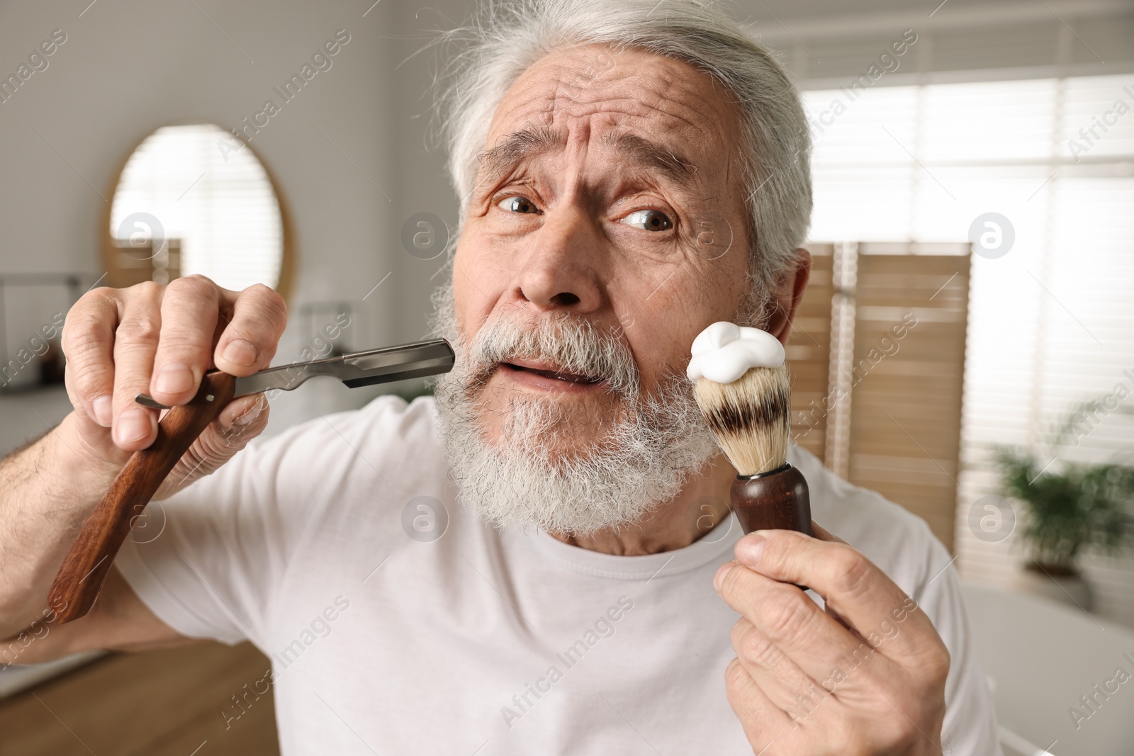 Photo of Man shaving mustache and beard with blade in bathroom