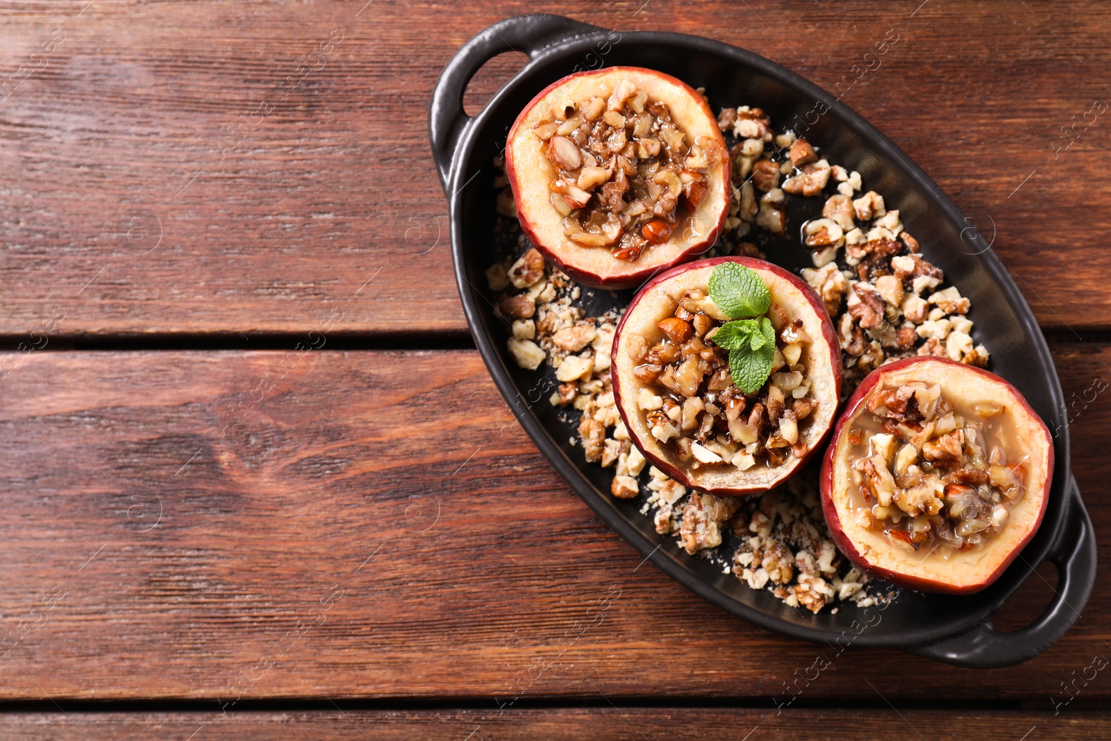 Photo of Tasty baked apples with nuts, honey and mint in baking dish on wooden table, top view. Space for text