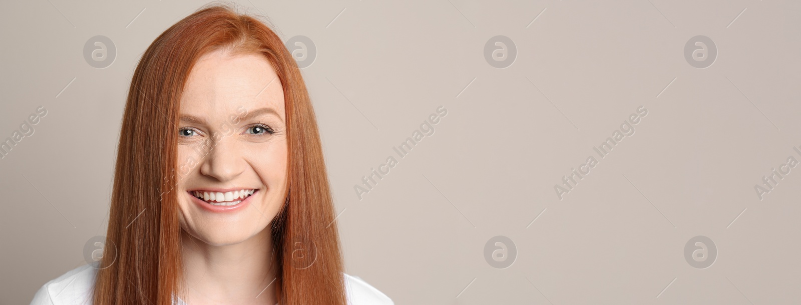 Photo of Candid portrait of happy young woman with charming smile and gorgeous red hair on beige background