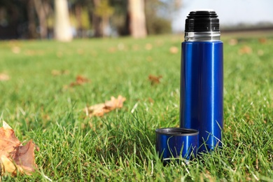 Photo of Modern blue thermos on green grass outdoors. Space for text