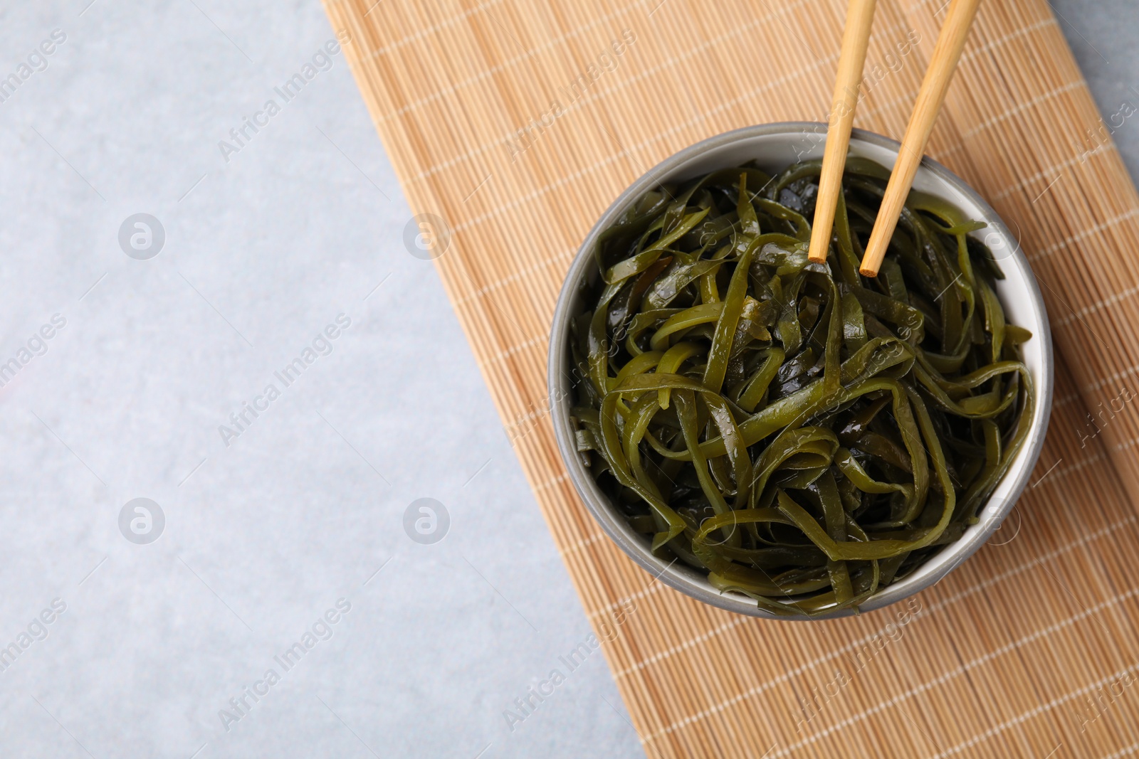 Photo of Tasty seaweed salad in bowl served on gray table, top view. Space for text