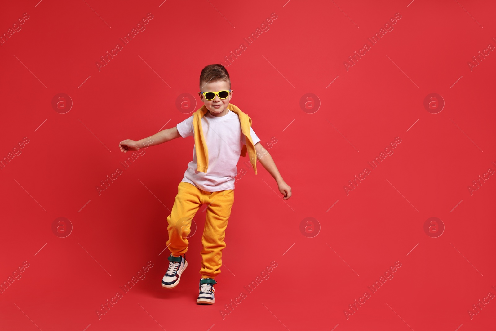 Photo of Happy little boy dancing on red background. Space for text