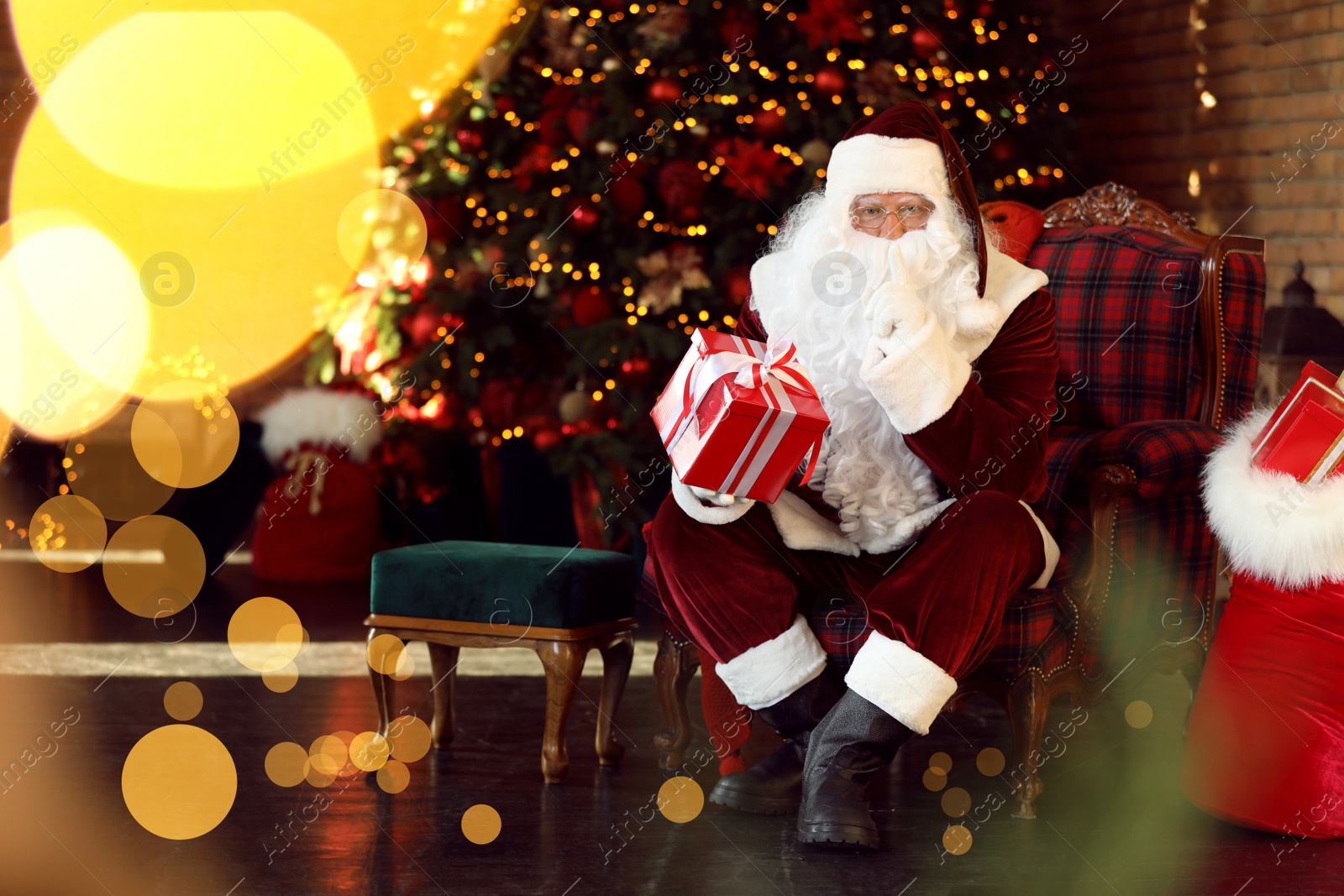 Photo of Santa Claus with gift near Christmas tree indoors