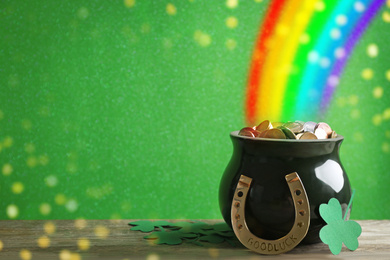 Image of Pot with gold coins, horseshoe and clover leaves on wooden table against green background, space for text. St. Patrick's Day celebration
