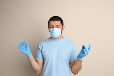 Photo of Man in protective mask meditating on beige background. Dealing with stress caused by COVID‑19 pandemic
