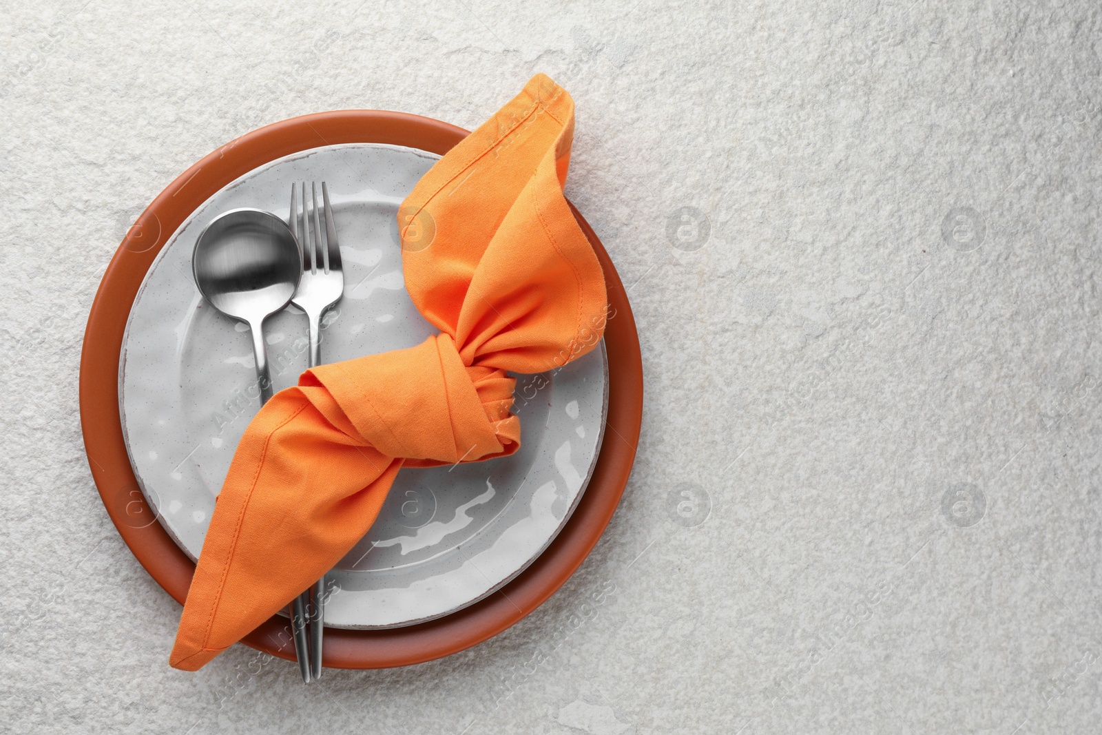 Photo of Stylish setting with cutlery, napkin and plates on light textured table, top view. Space for text