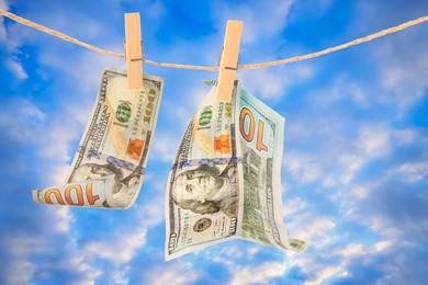 Image of Money laundering. Dollar banknotes hanging on clothesline against blue sky