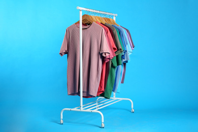 Photo of Colorful clothes hanging on rack against light blue background