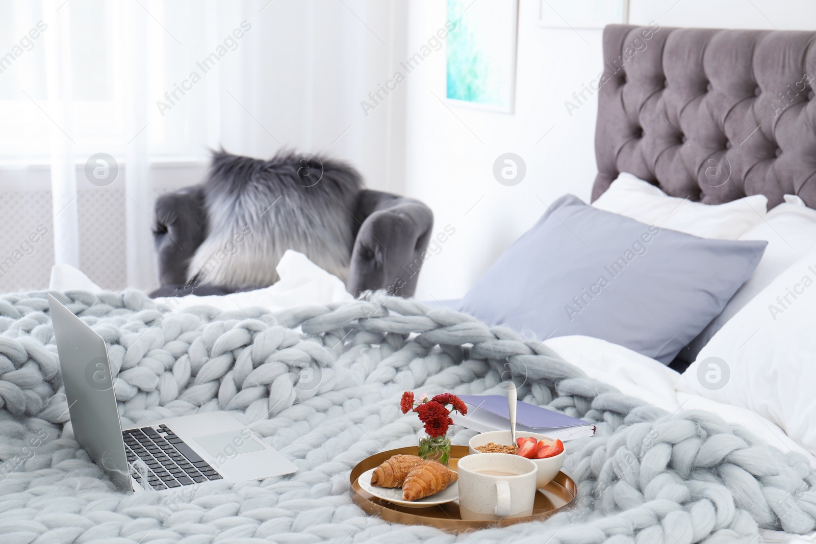 Photo of Laptop, notebook and tray with breakfast on bed in stylish room interior