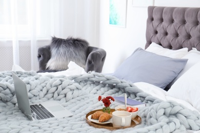 Laptop, notebook and tray with breakfast on bed in stylish room interior