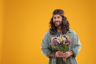 Hippie man with bouquet of colorful flowers showing V-sign on orange background, space for text