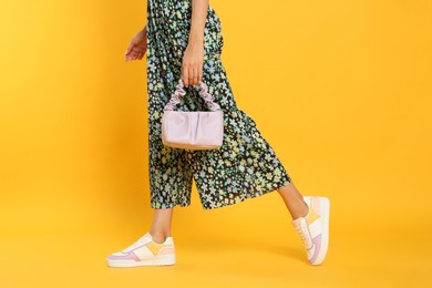 Woman with stylish bag on yellow background, closeup