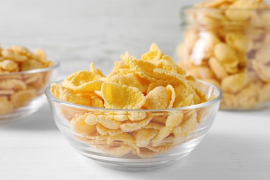 Photo of Glass bowl of tasty crispy corn flakes on white wooden table, closeup