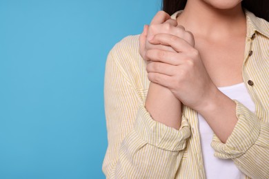 Young woman suffering from pain in hands on light blue background, closeup with space for text. Arthritis symptoms